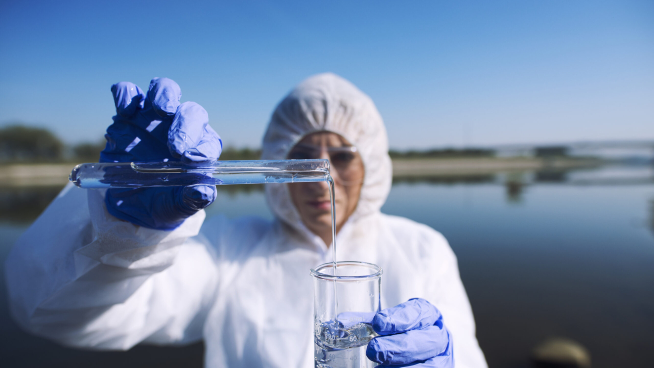 Ecologist sampling water from the river with test tube.